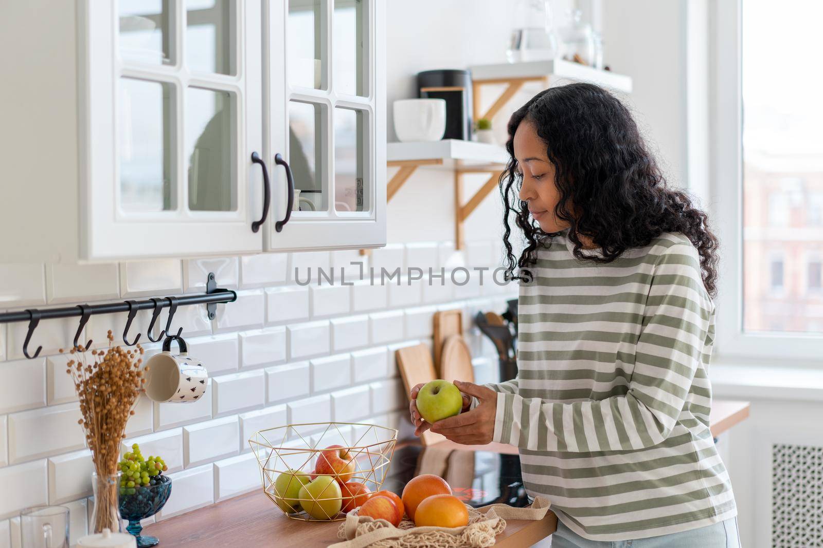 African-american woman sorting green and red apples, oranges. Concept of healthy vegan products. Dietary fruits and citrus. Sweet nutritious snack. Choosing food for cooking breakfast. Horizontal