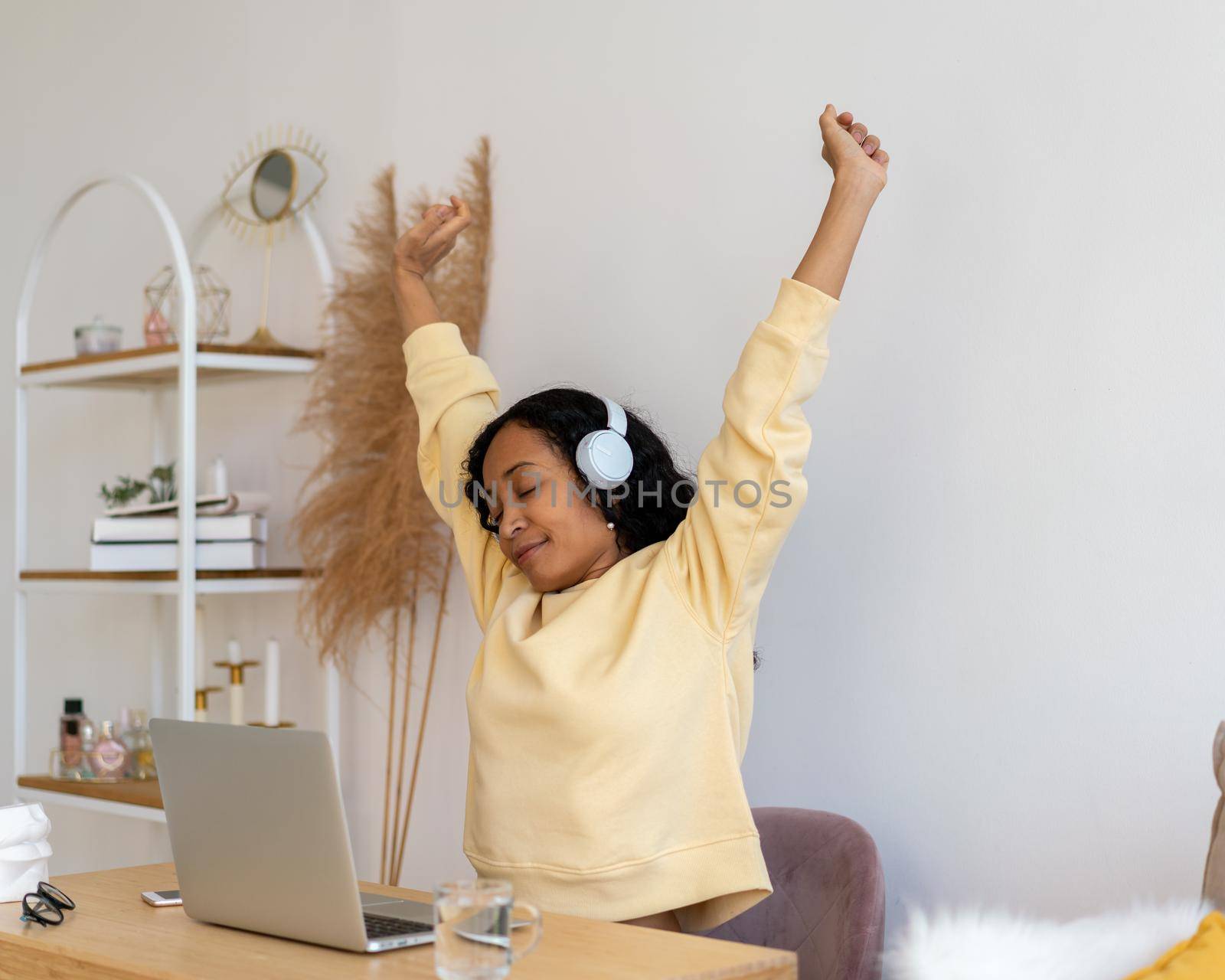 African-american female stretching after working on laptop. Listening to music in earphones by NataBene