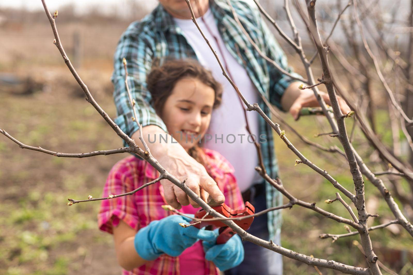 A small girl with grandfather outside in spring nature, having fun. gardening by Andelov13