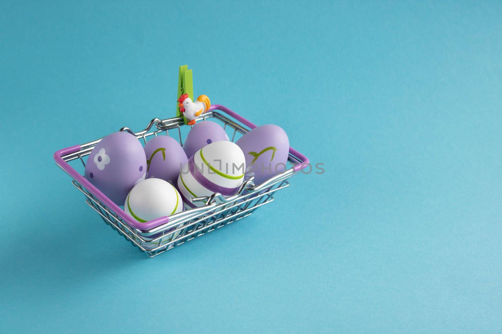 Metal shopping basket with lilac chicken eggs on a blue background. Dietary fresh product. Easter concept. Place for your text by lapushka62
