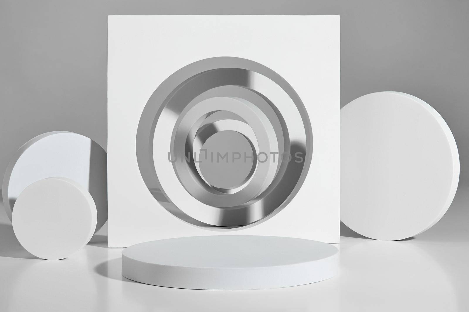 Abstract podium design for product display consisting of empty platform, vertically arranged flat cylinders and rings and round cut square element. White geometrical shapes on gray background