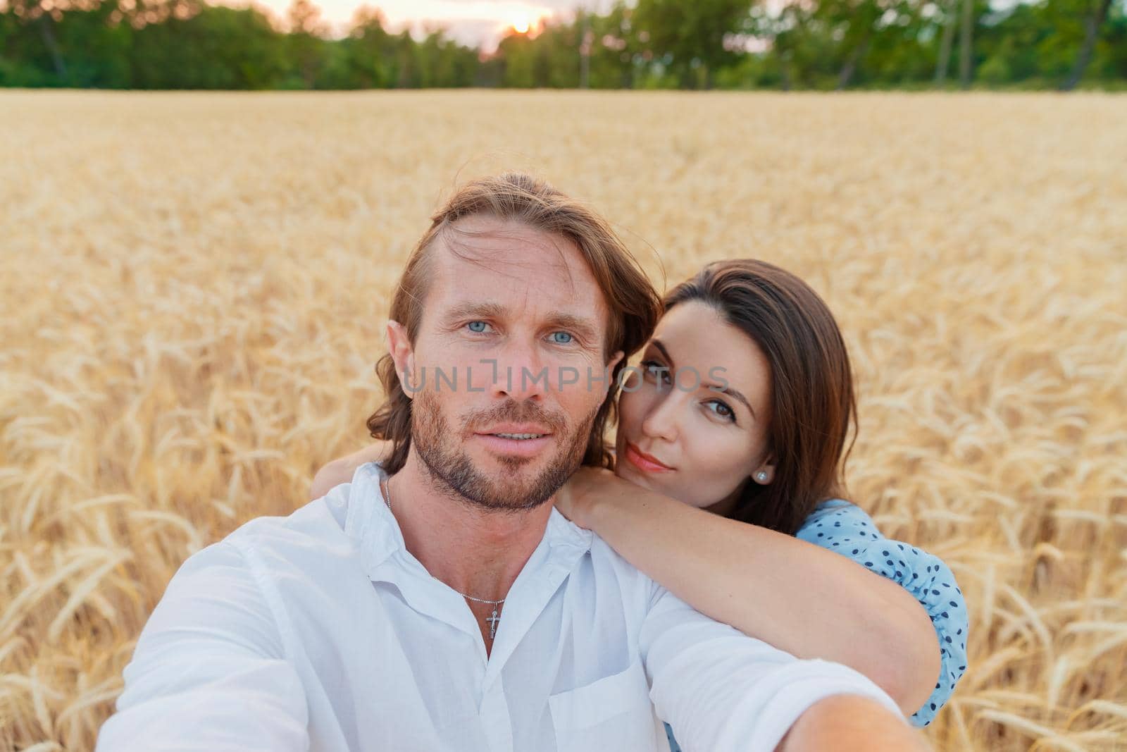 The beautiful couple embraces in the field of a wheat at sunset, they are happy, the long hair, an easy beard, wheat ears on background, blue dress and white shirt. High quality photo
