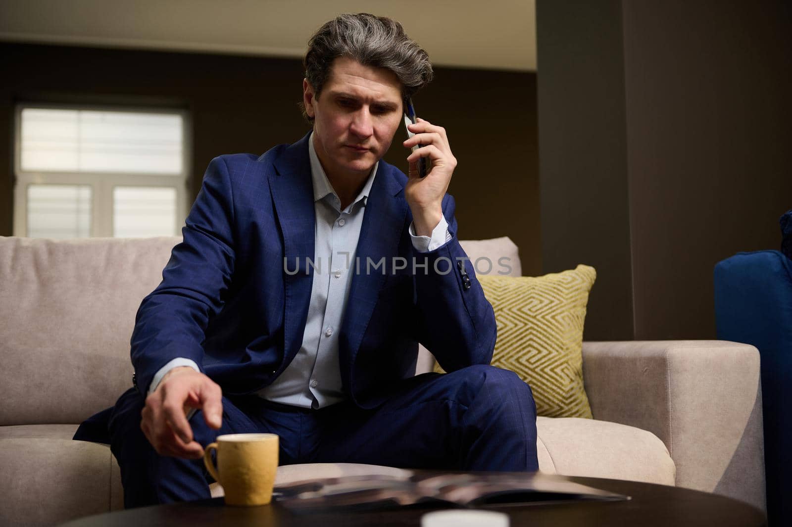 Portrait of a mature successful businessman talking on a mobile phone during a coffee break in his office. Handsome imposing entrepreneur, sales manager negotiating and advising clients on the phone