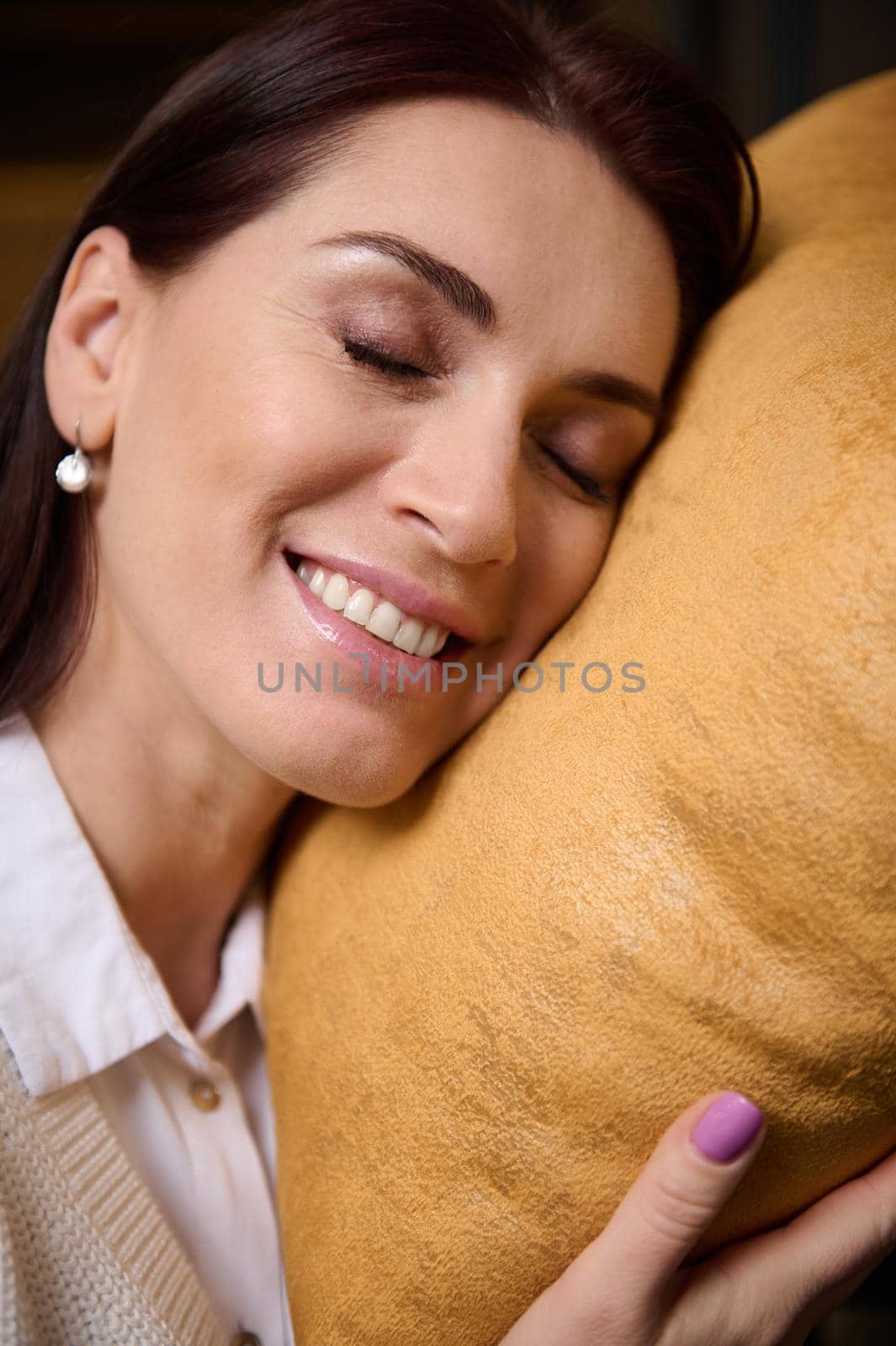Close-up of a delightful beautiful relaxed serene middle-aged European woman with closed eyes leaning her head on a velour pillow. Healthy pleasant sleep and home interior design concept