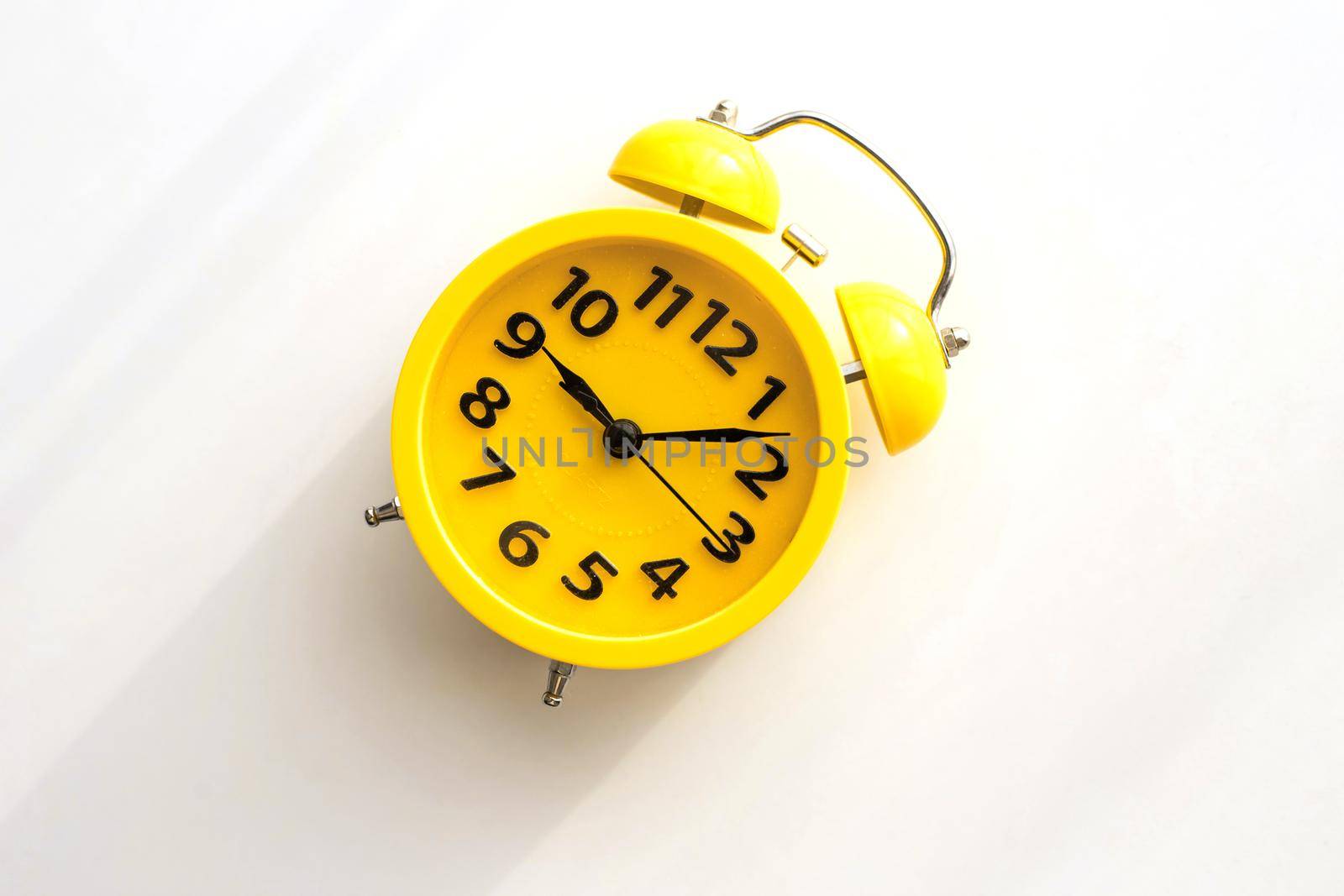A yellow retro alarm clock with a black dial lies on a white table diagonally to the left. view from above. copy space