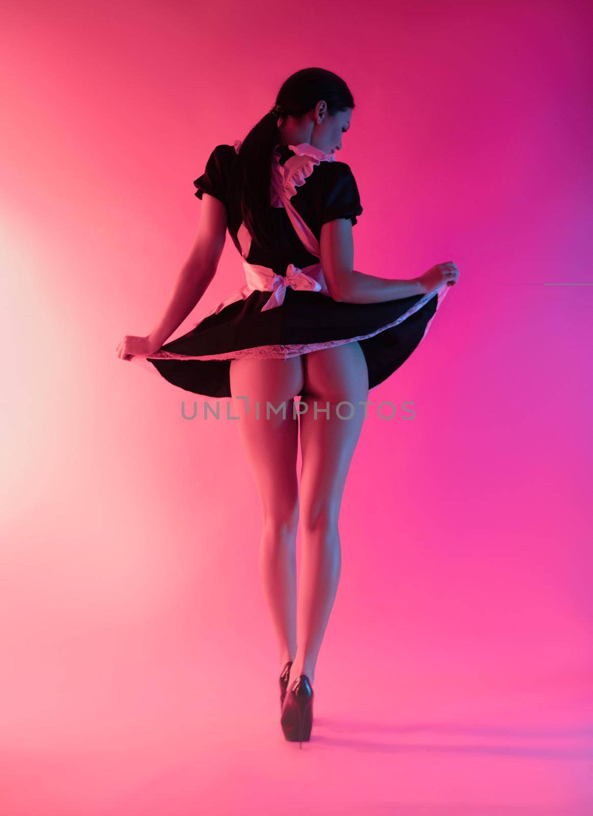 a sexy girl in a maid costume stands with her back exposing her buttocks in neon light on an empty background