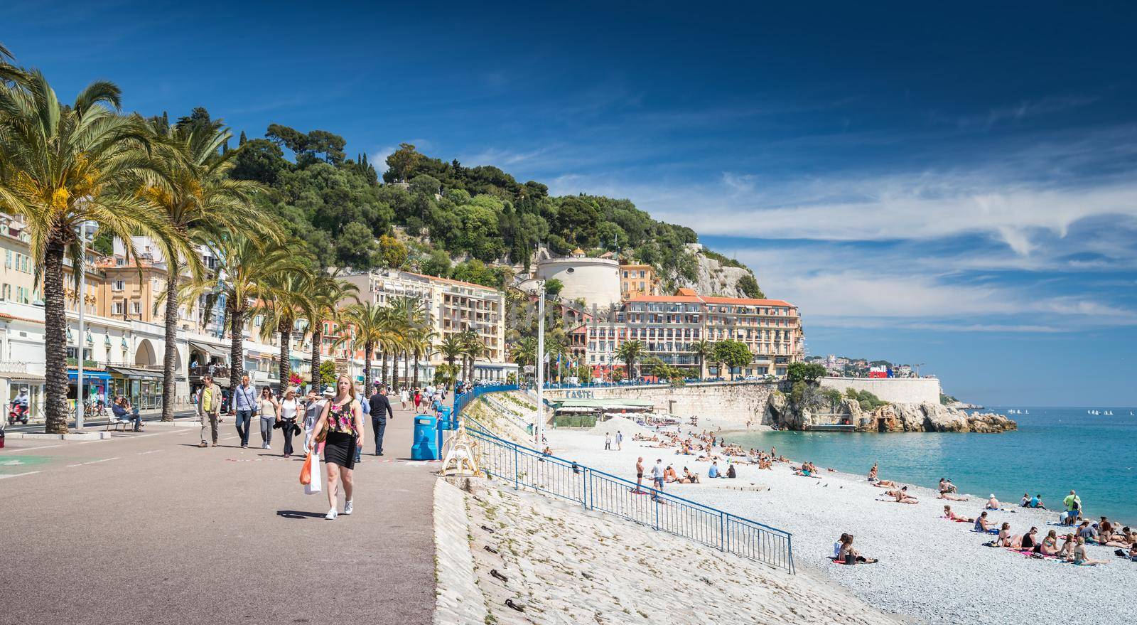 France, Nice, 15 May 2017: Promenade Anglais, Beautiful Public Beach, Tourists, Sunbath People, Swim, Sunny Day, People sit on the well-known blue chairs. High quality photo