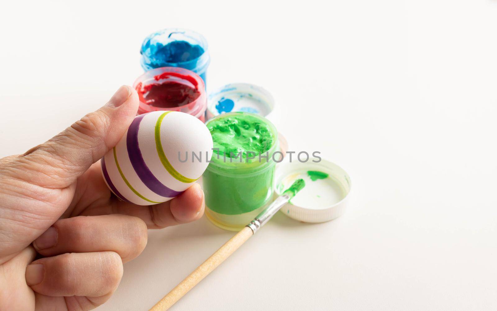 The hand holds a white egg for coloring. The process of painting an Easter egg with light green paint. The tradition and concept of Easter. Spring season April holidays. Place for your text by lapushka62