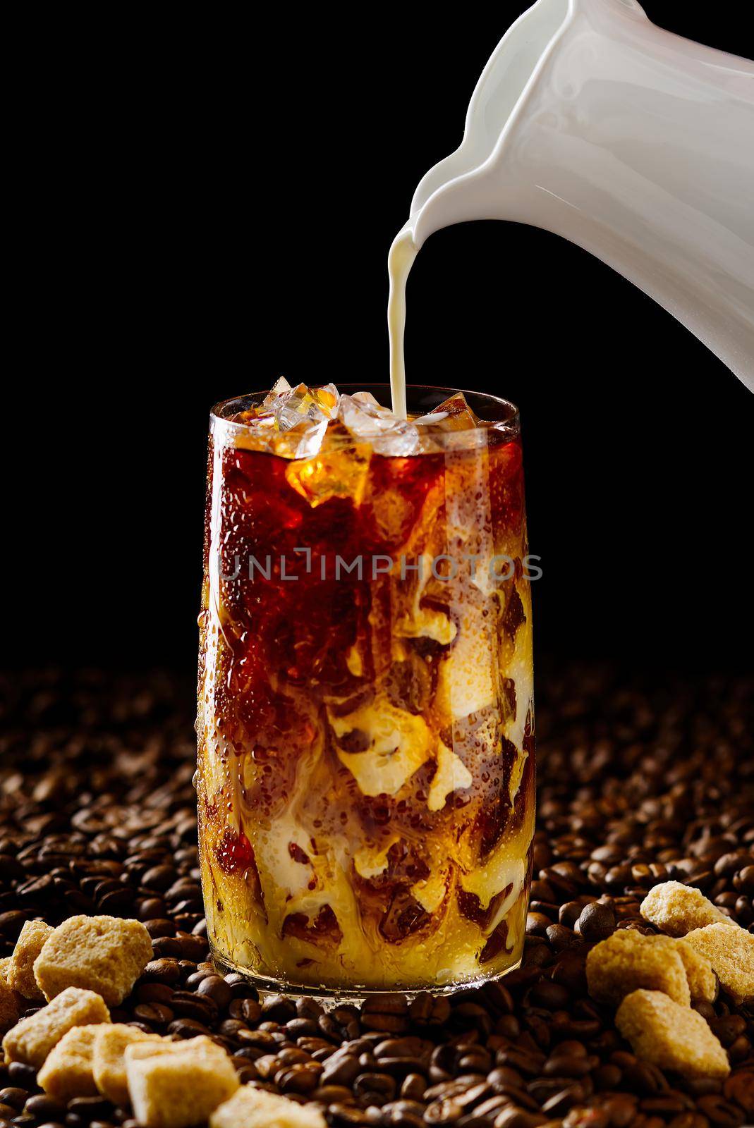 Tasty Iced coffee. Tasty ice coffee with milk, cold drink in glass with ice on dark coffee background Copy space.