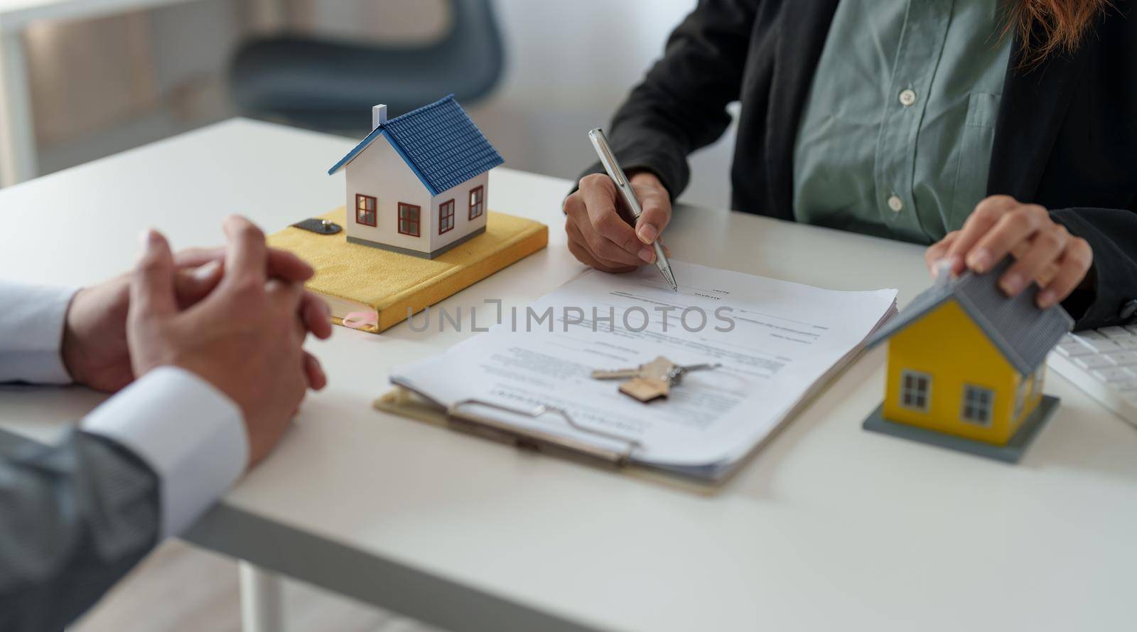 Real estate agent assisting client to sign contract at desk with house model by nateemee