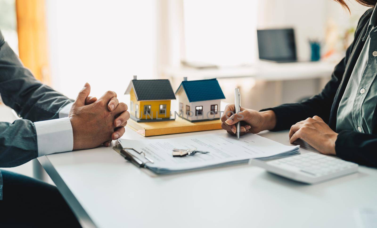 Real estate agent assisting client to sign contract at desk with house model by nateemee