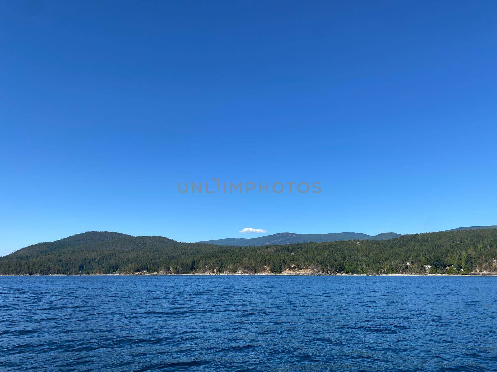 View of Sunshine Coast mountains from the water with blue skies and blue water, British Columbia