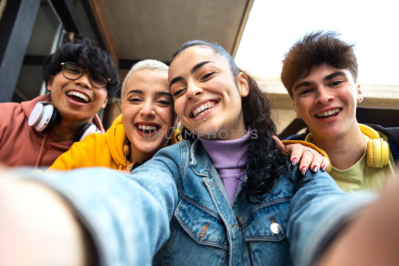 Smiling multiracial group of friends take selfie with phone outside university building. Students laughing and having fun. Youth lifestyle and social media concept.