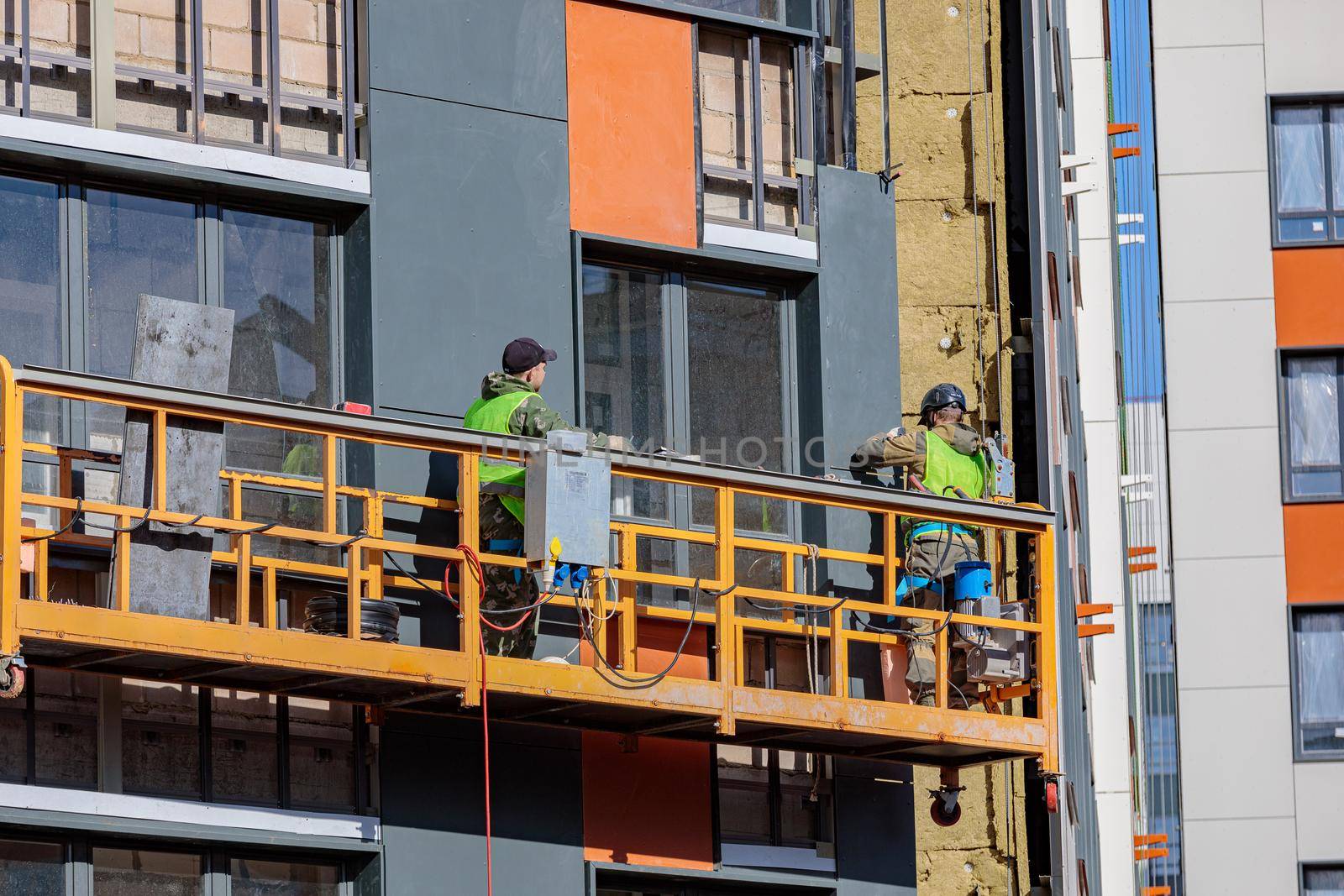 Male builders work on the facade of the building in a suspended cradle. Construction works. Moscow Russia April 14, 2022