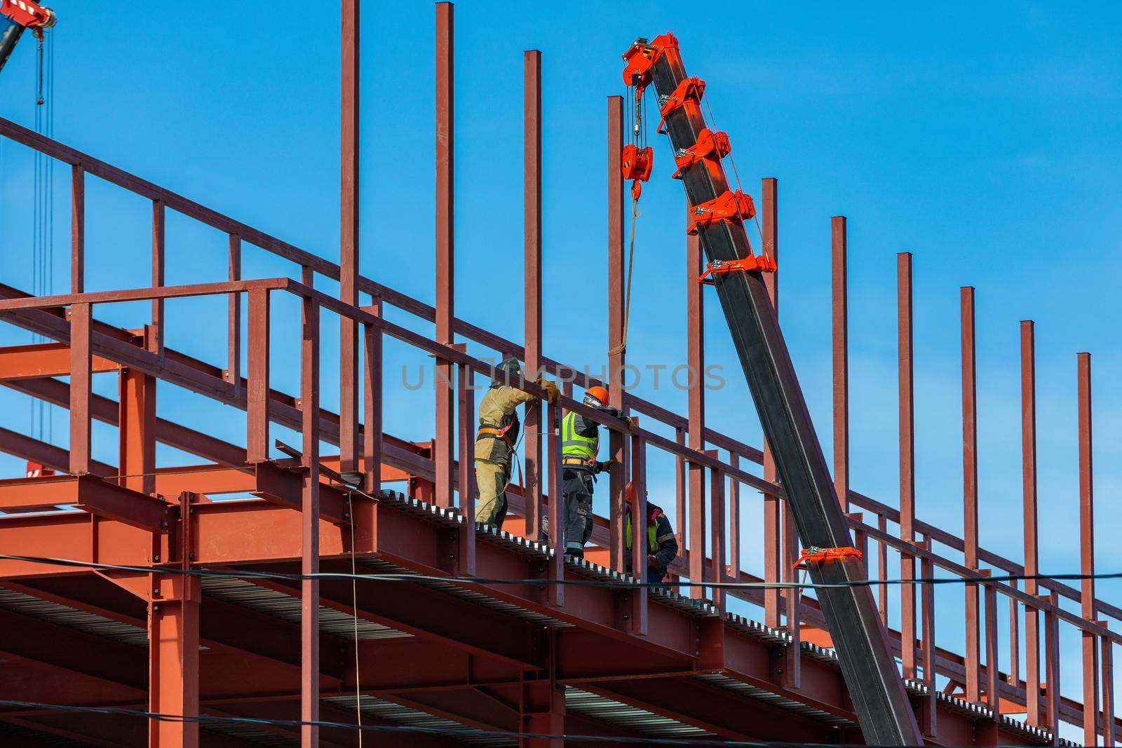 Builders fix iron beams with a crane. Frame construction.