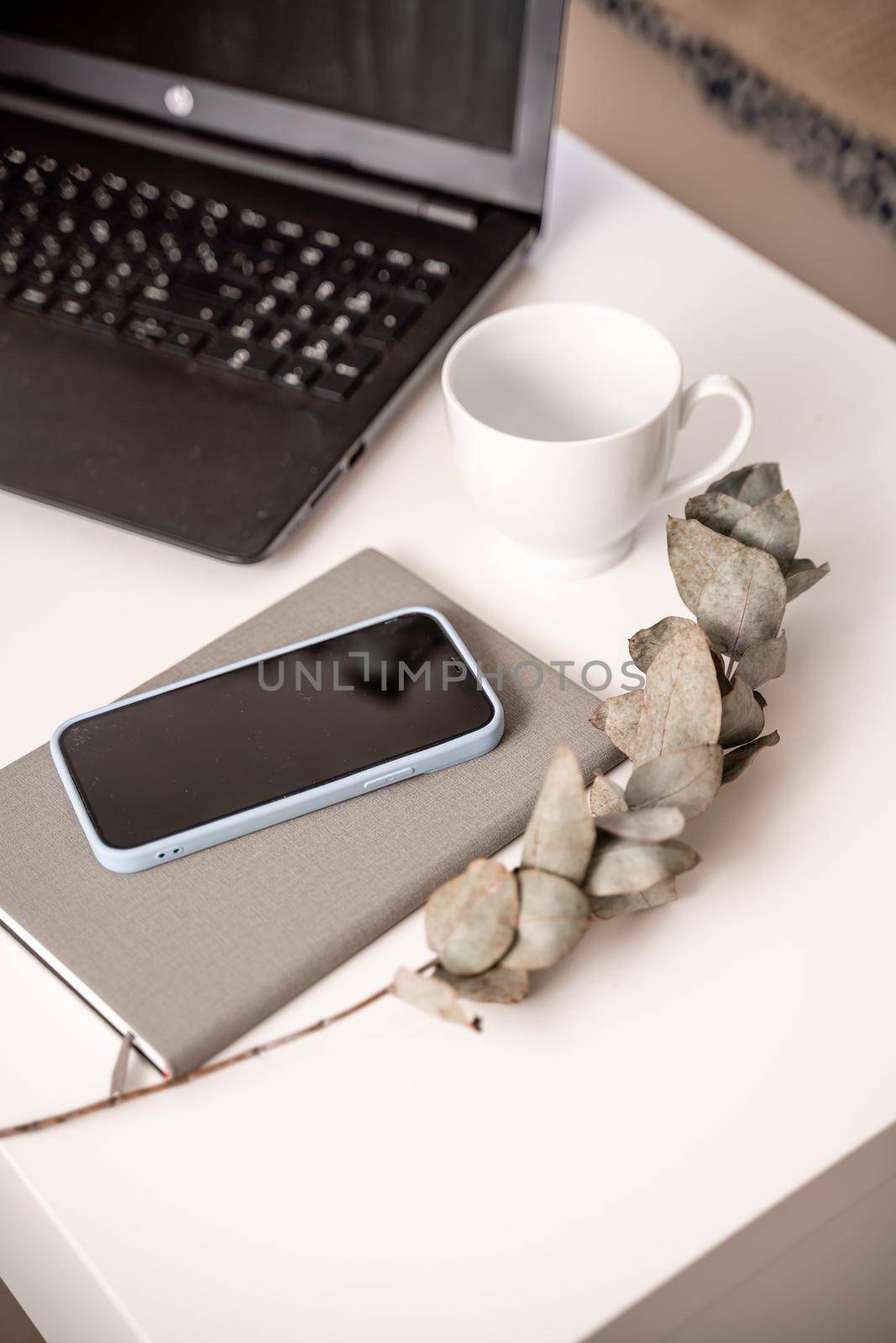 White desktop with laptop, coffee mug, phone and notebook for remote work or study. Office computer workplace in home interior.