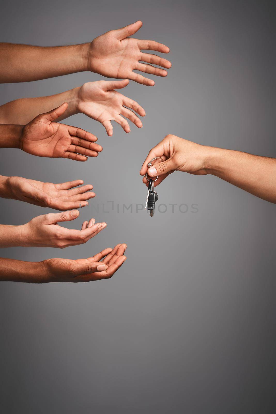 Studio shot of unidentifiable hands reaching for a set of keys against a gray background.