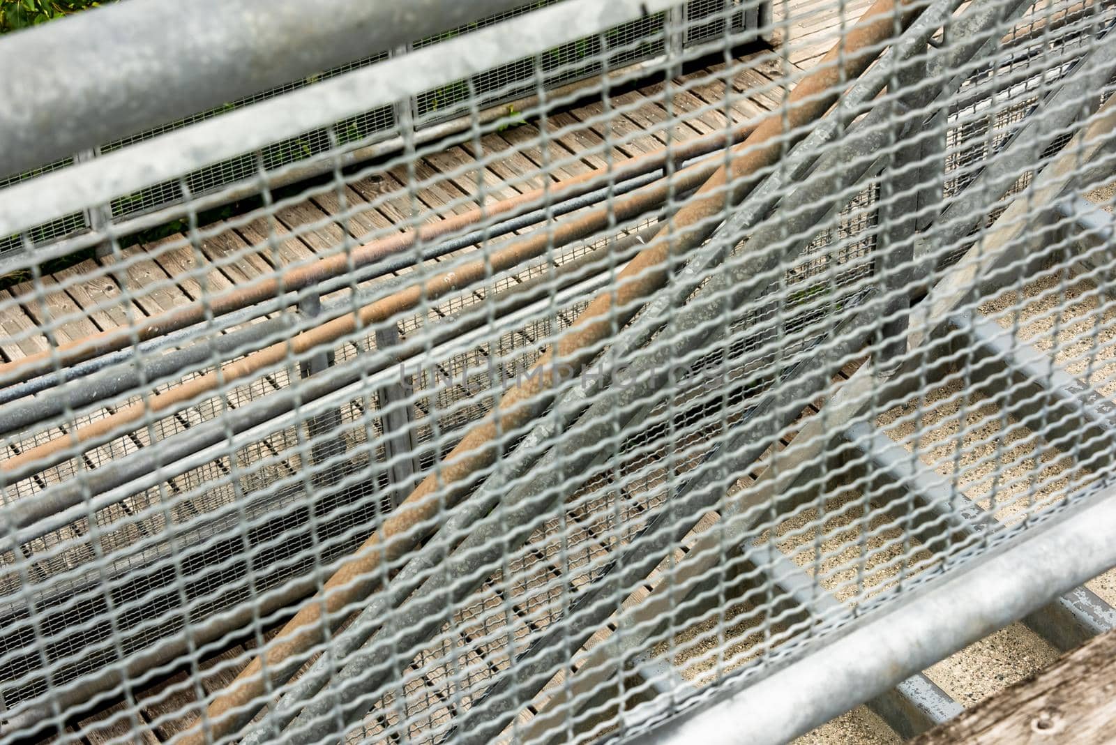 Abstract look through the metal grid on stairs and wooden deck in a park. Texture background