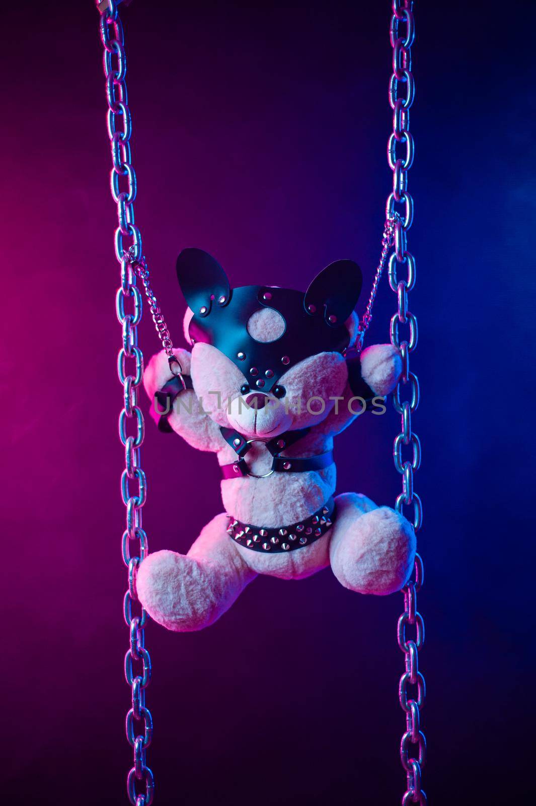 the toy bear dressed in leather belts harness accessory for BDSM games on a dark background in neon light