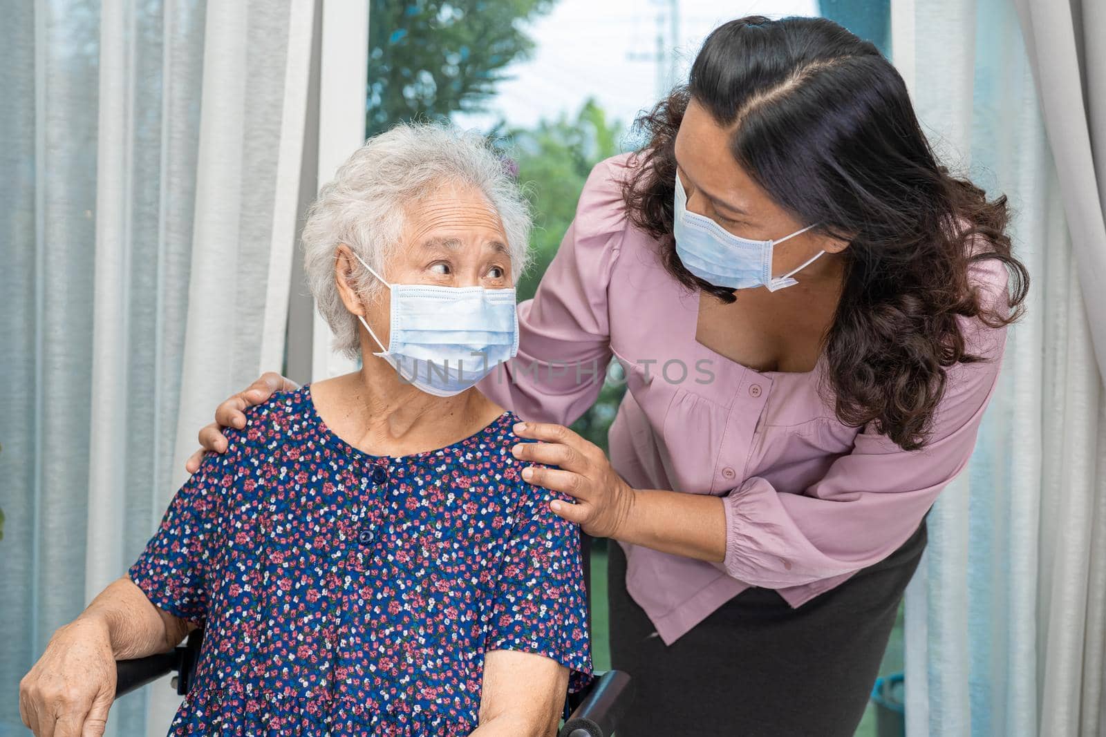 Caregiver help Asian senior or elderly old lady woman sitting on wheelchair and wearing a face mask for protect safety infection Covid19 Coronavirus. by pamai