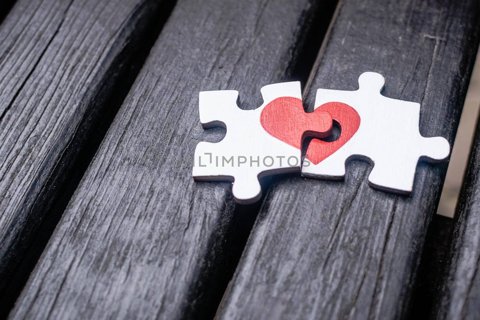 Red heart is drawn on the pieces of the wooden puzzle lying next to each other on wooden background. Love concept.