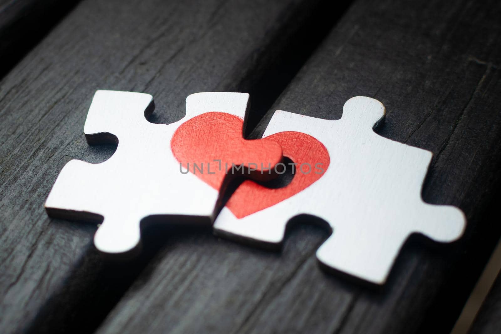 Red heart is drawn on the pieces of the wooden puzzle lying next to each other on wooden background. Love concept.