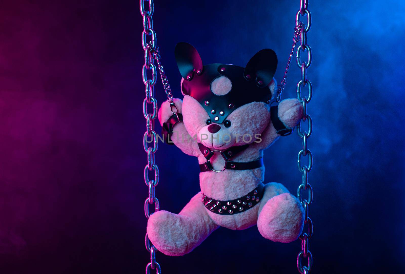 toy bear dressed in leather belts harness accessory for BDSM games on a dark background in neon light by Rotozey