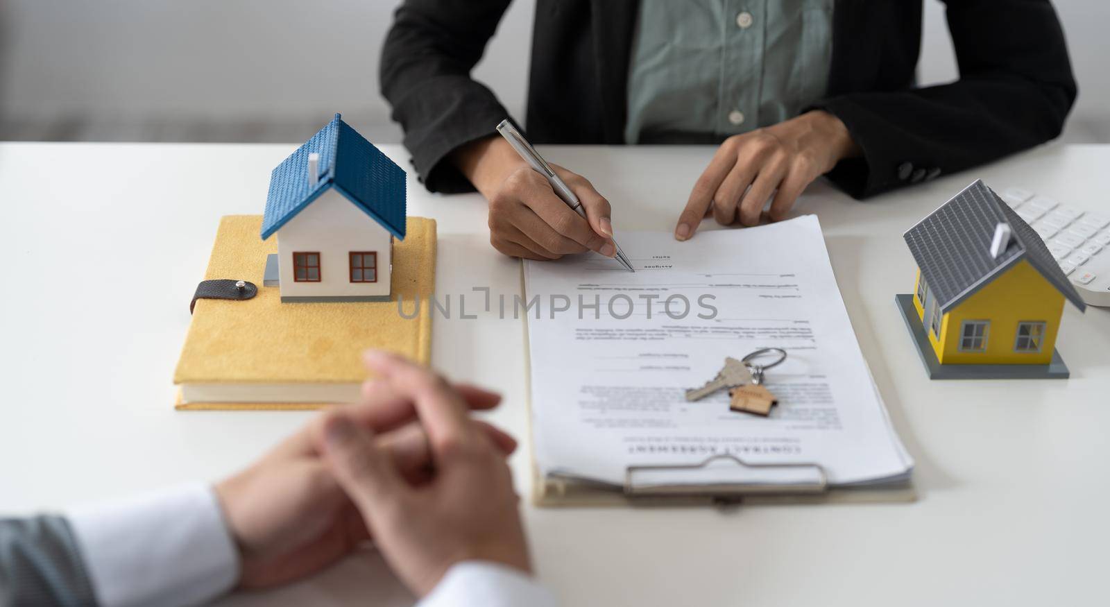 Real estate agent assisting client to sign contract at desk with house model by nateemee