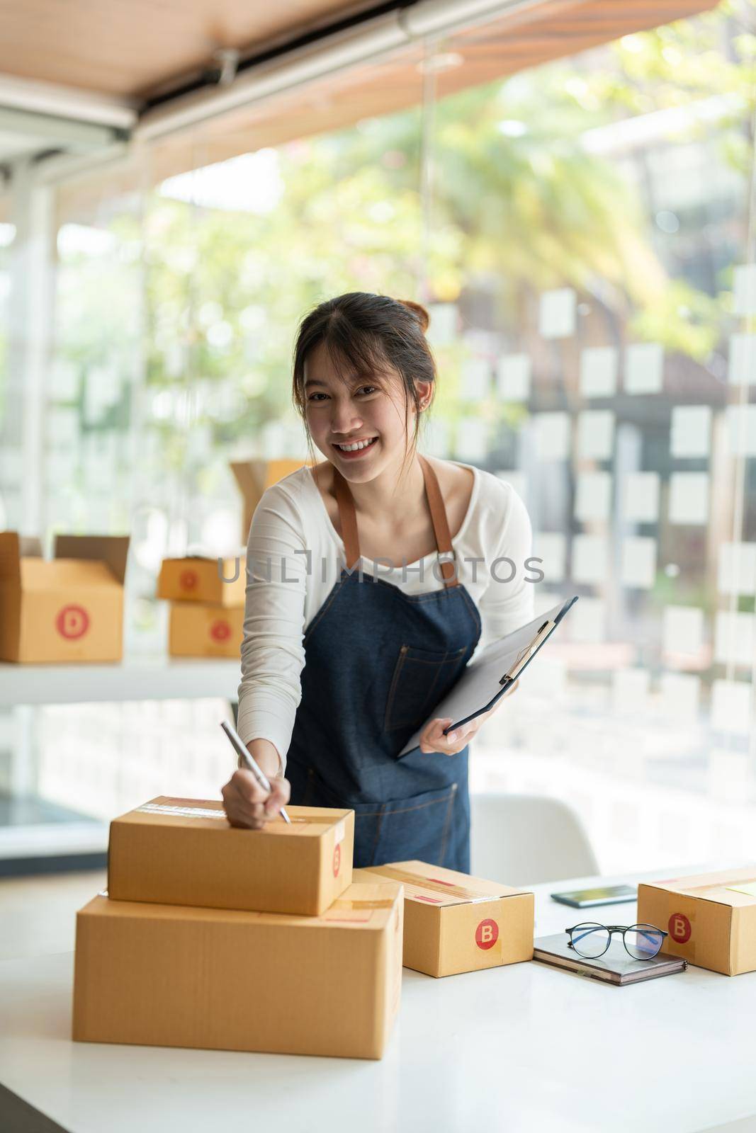 Portrait young attractive asia female owner startup look at camera work happy with box at home prepare parcel delivery in sme supply chain, procurement, omnichannel ecommerce online concept