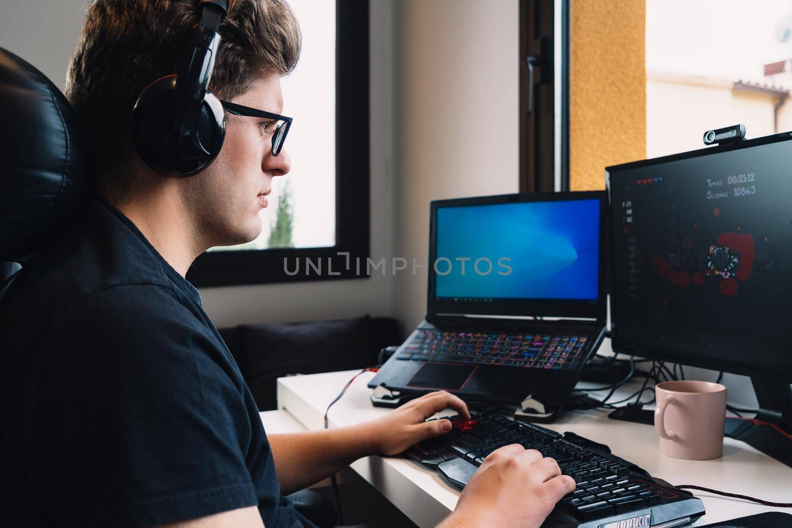 young blond man listening to music through headphones on computer sitting at desk. by CatPhotography