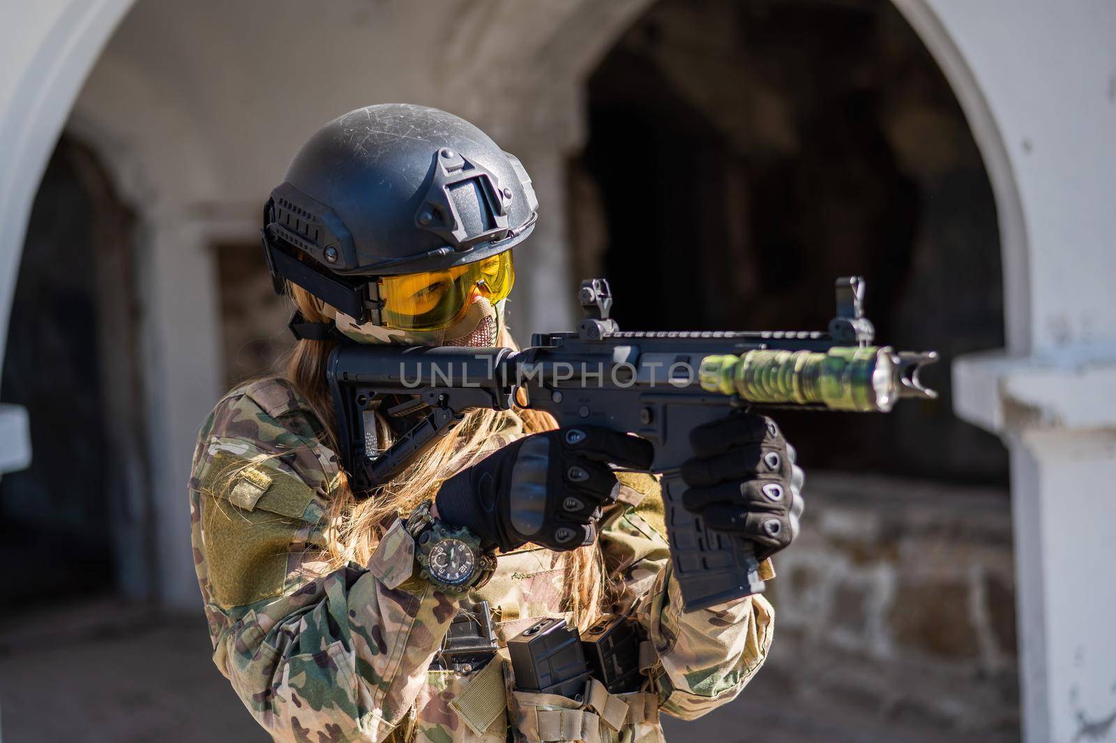 Caucasian woman in a protective suit with a machine gun. FA female soldier in a camouflage uniform holds a weapon