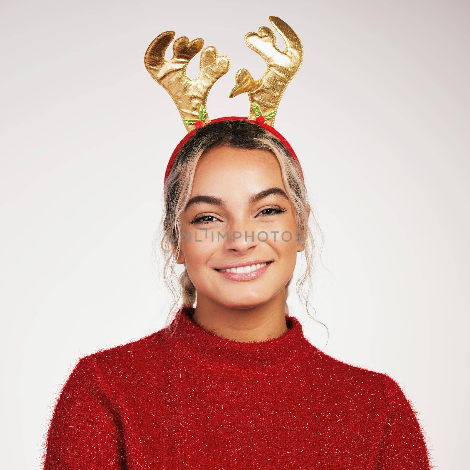 Studio shot of a young woman wearing a reindeer headwear against a grey background.