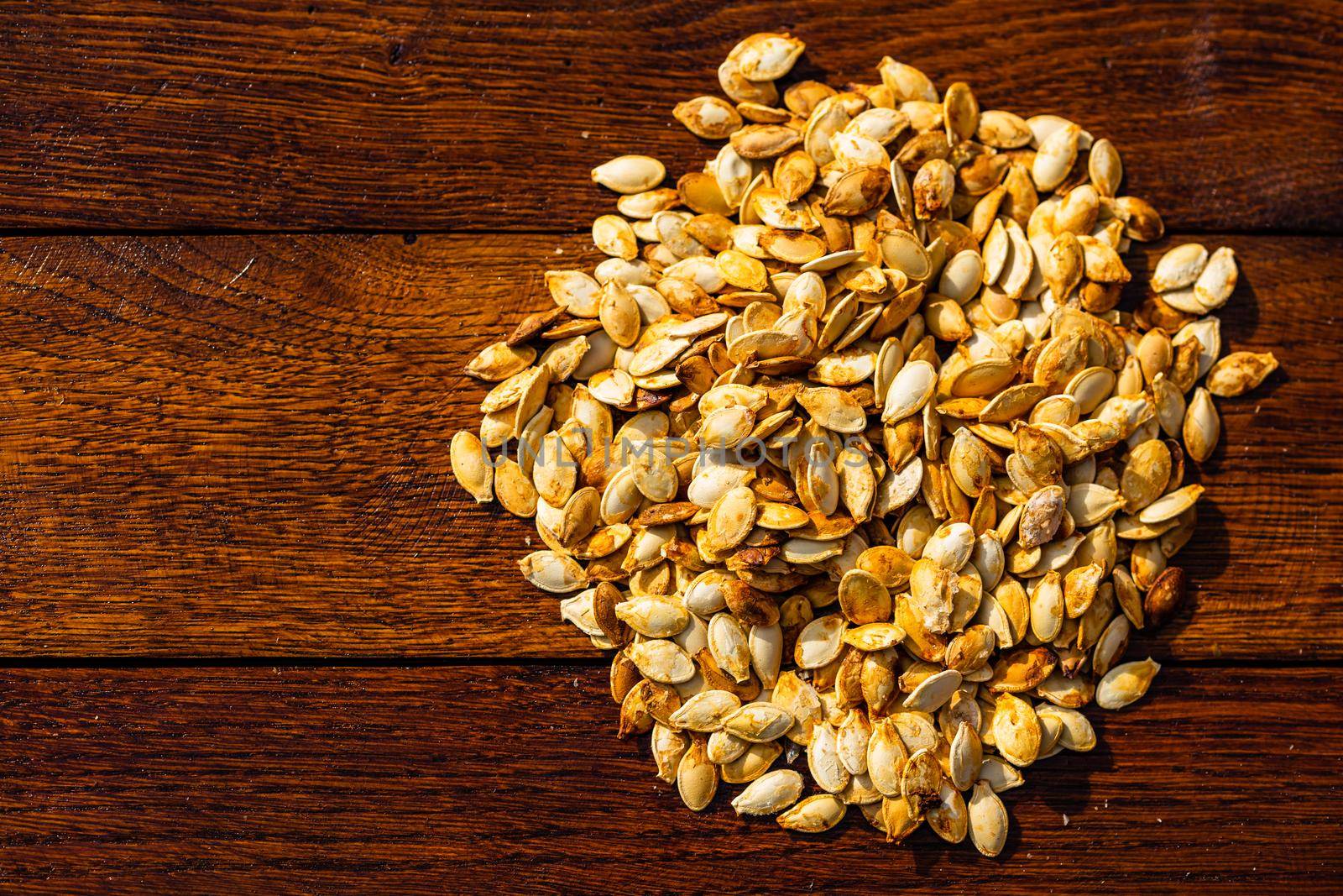 Roasted and salted pumpkin seeds on a wooden board.