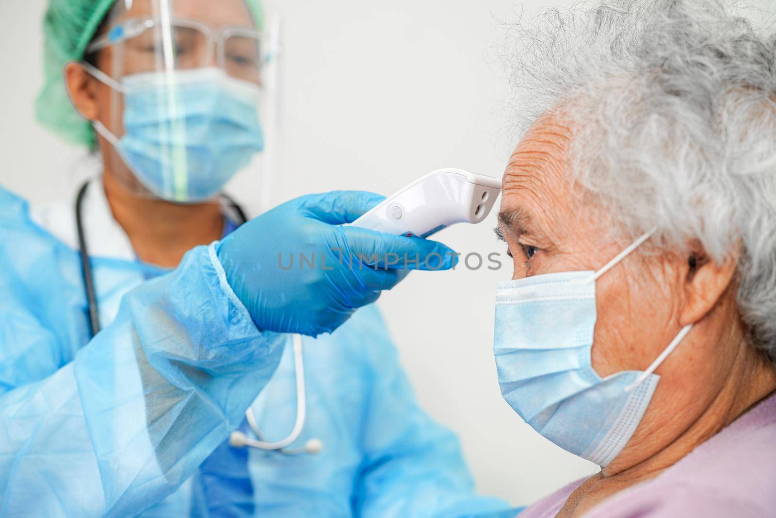 Doctor in ppe user infrared thermometer to check temperature of asian elderly woman patient for safety to protect covid 19 virus.