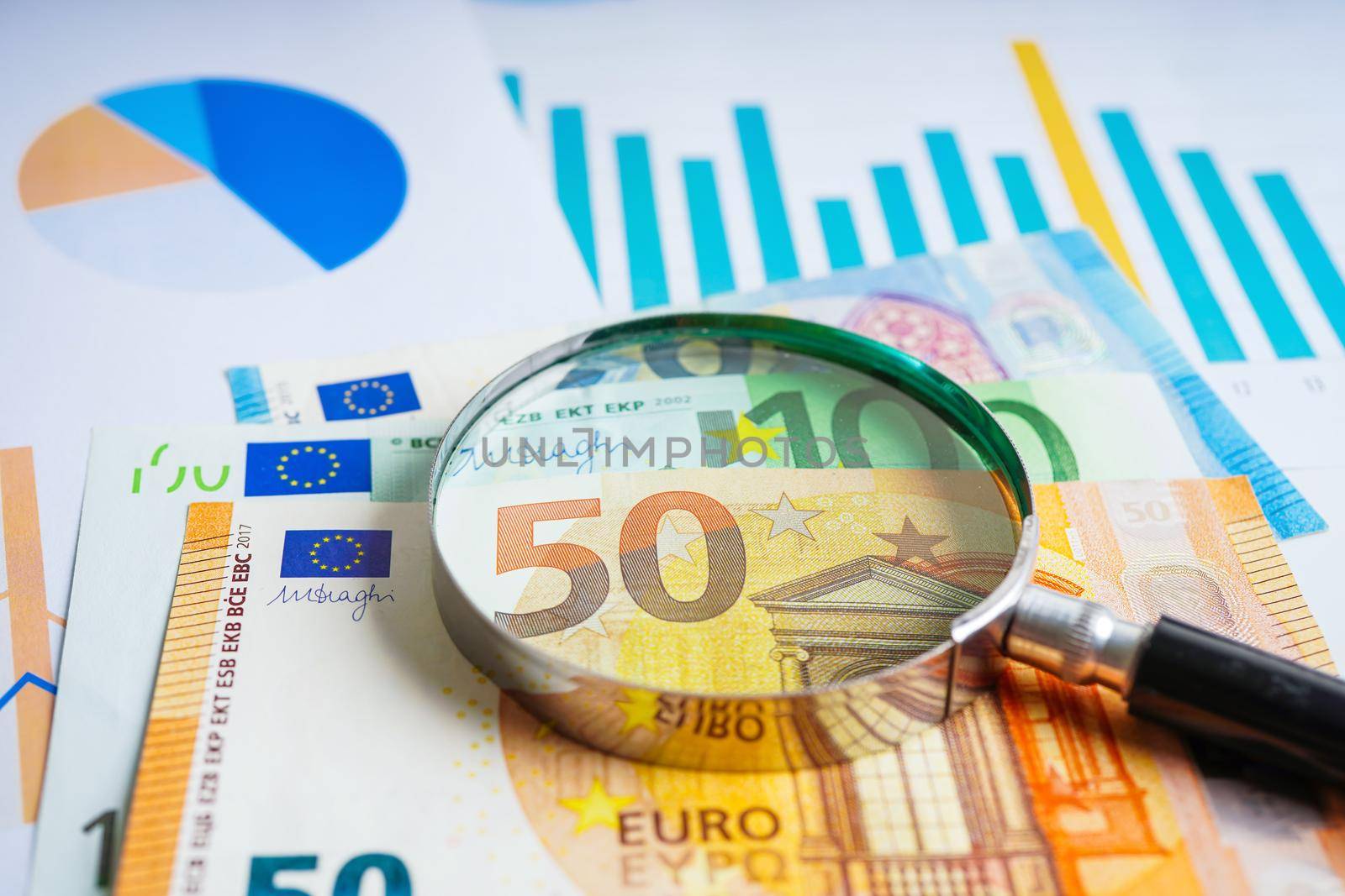 Magnifying glass on EURO banknotes and graph, finance business trade concept.