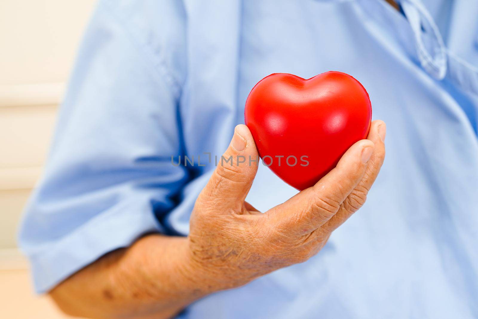 Asian elder senior woman patient holding red heart in hospital.  