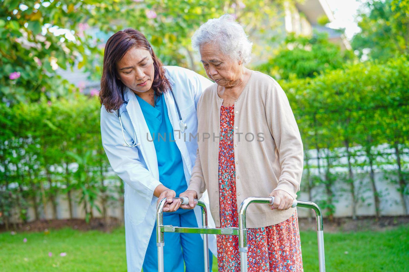 Caregiver help Asian elderly woman disability patient walk with walker in park, medical concept.