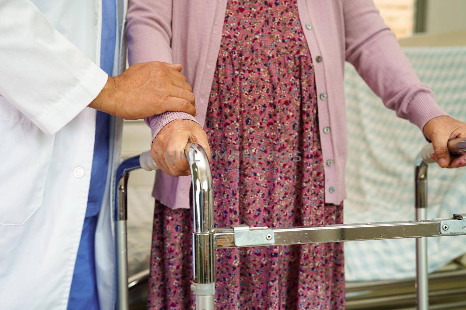 Doctor help Asian elderly woman disability patient walk with walker in nursing hospital, medical concept.