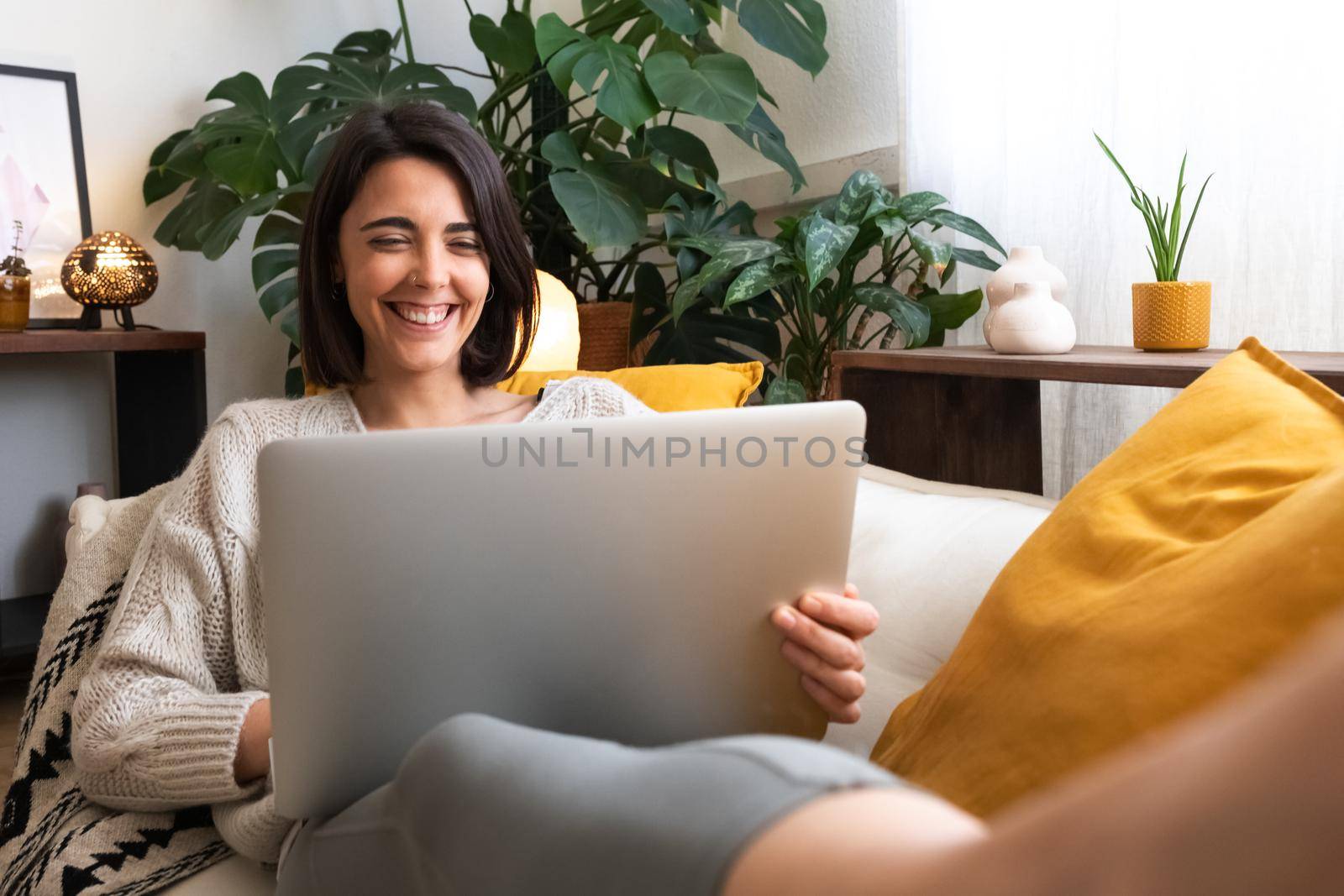 Happy, smiling young caucasian woman using laptop lying on couch at home cozy living room. Copy space. Lifestyle and technology concept.