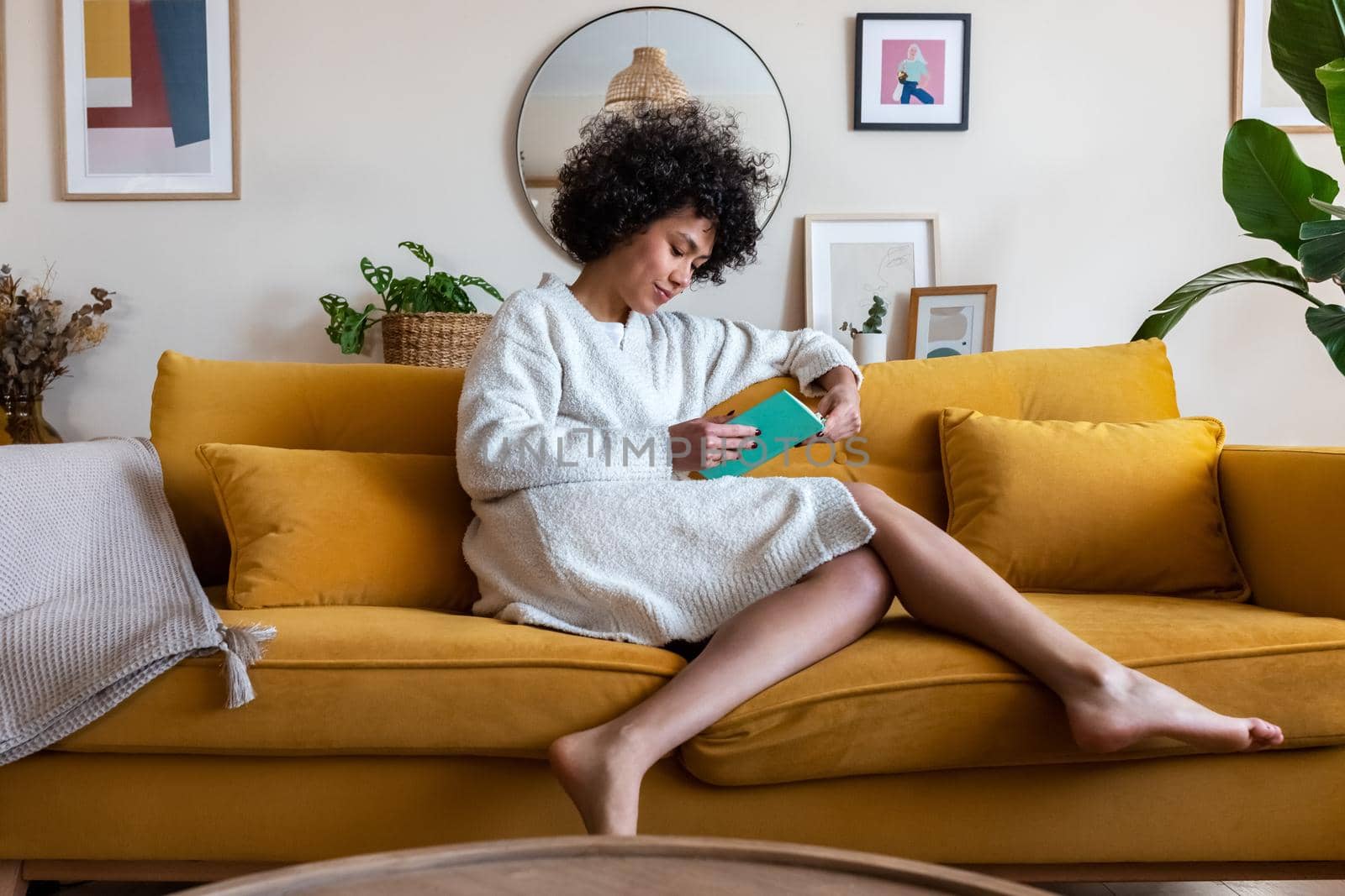 African american woman relaxing at home reading a book sitting on couch. Literature and lifestyle concept.