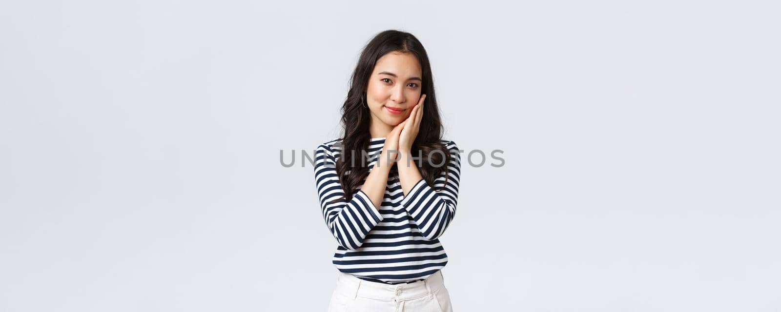 Lifestyle, people emotions and casual concept. Tender asian woman with beautiful face, touching cheek gently and gazing camera, advertising beauty product, cosmetics or skincare items.