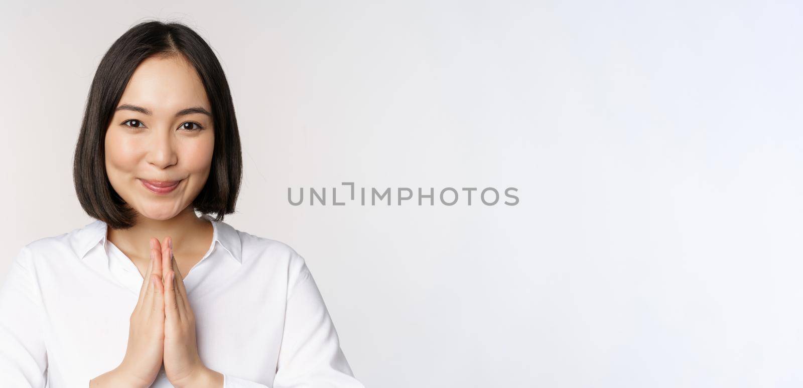 Close up portrait of young japanese woman showing namaste, thank you arigatou gesture, standing over white background.
