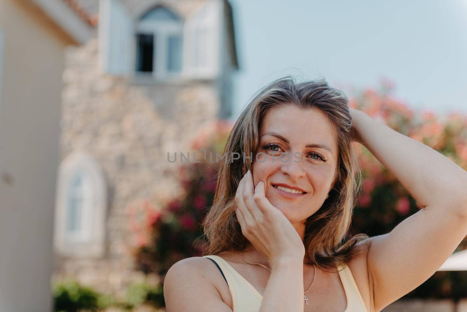 Girl Tourist Walking Through Ancient Narrow Street On A Beautiful Summer Day In MEDITERRANEAN MEDIEVAL CITY, OLD TOWN BUDVA, MONTENEGRO. Young Beautiful Cheerful Woman Walking On Old Street At Tropical Town. Pretty Girl Looking At You And Smiling by Andrii_Ko