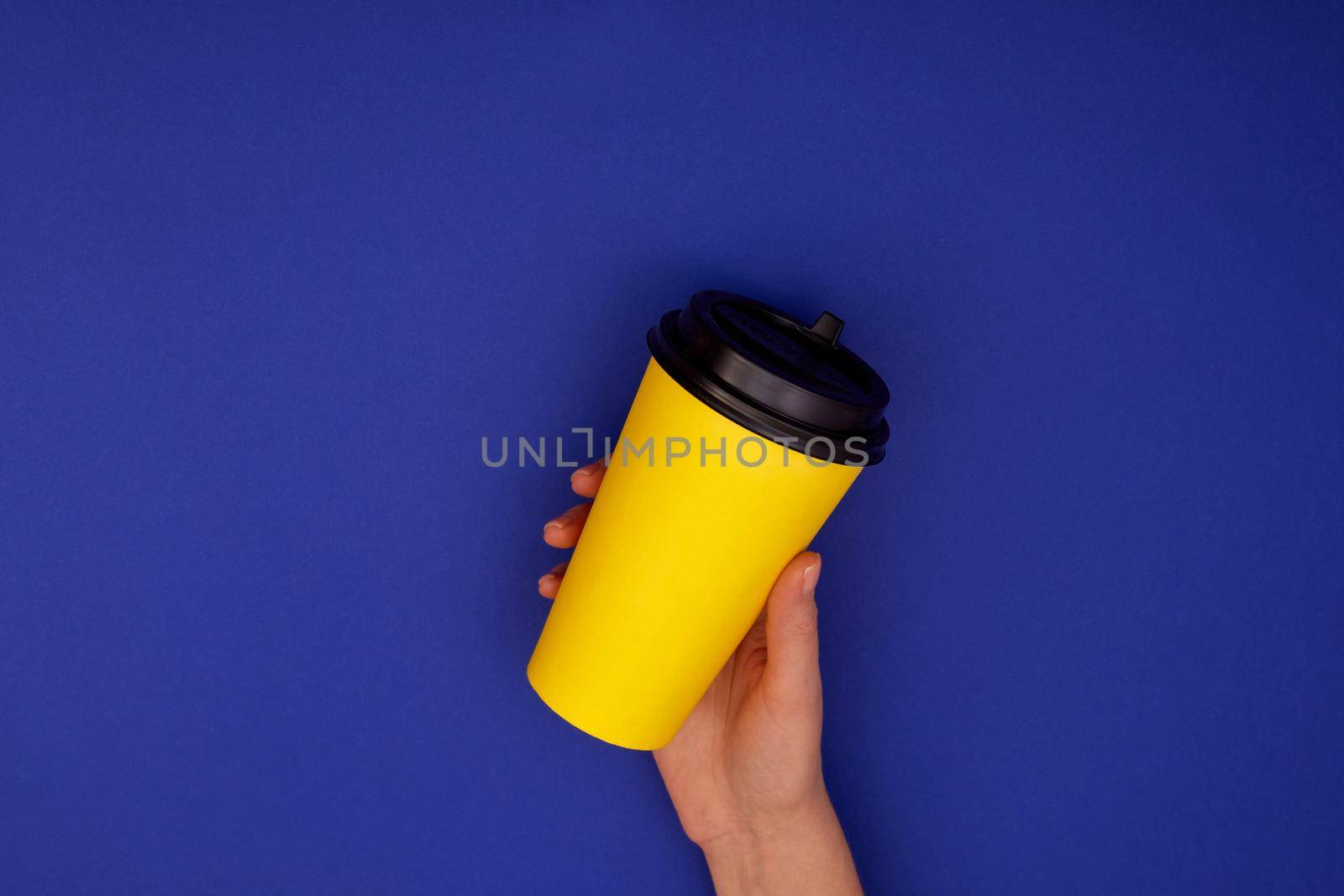 Paper cup of coffee in hand. Yellow paper cup of coffee in hand isolated mock up dark blue background