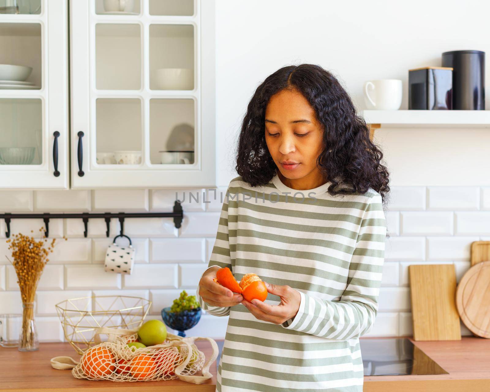 African-American female checking orange citrus for spoilage in kitchen after grocery shopping by NataBene