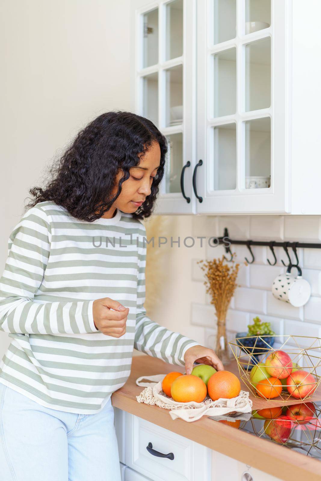 Female African-American woman taking out fruit bought at grocery store. Using eco-bags for shopping trips. Concept of healthy food and eco-friendly sustainable lifestyle
