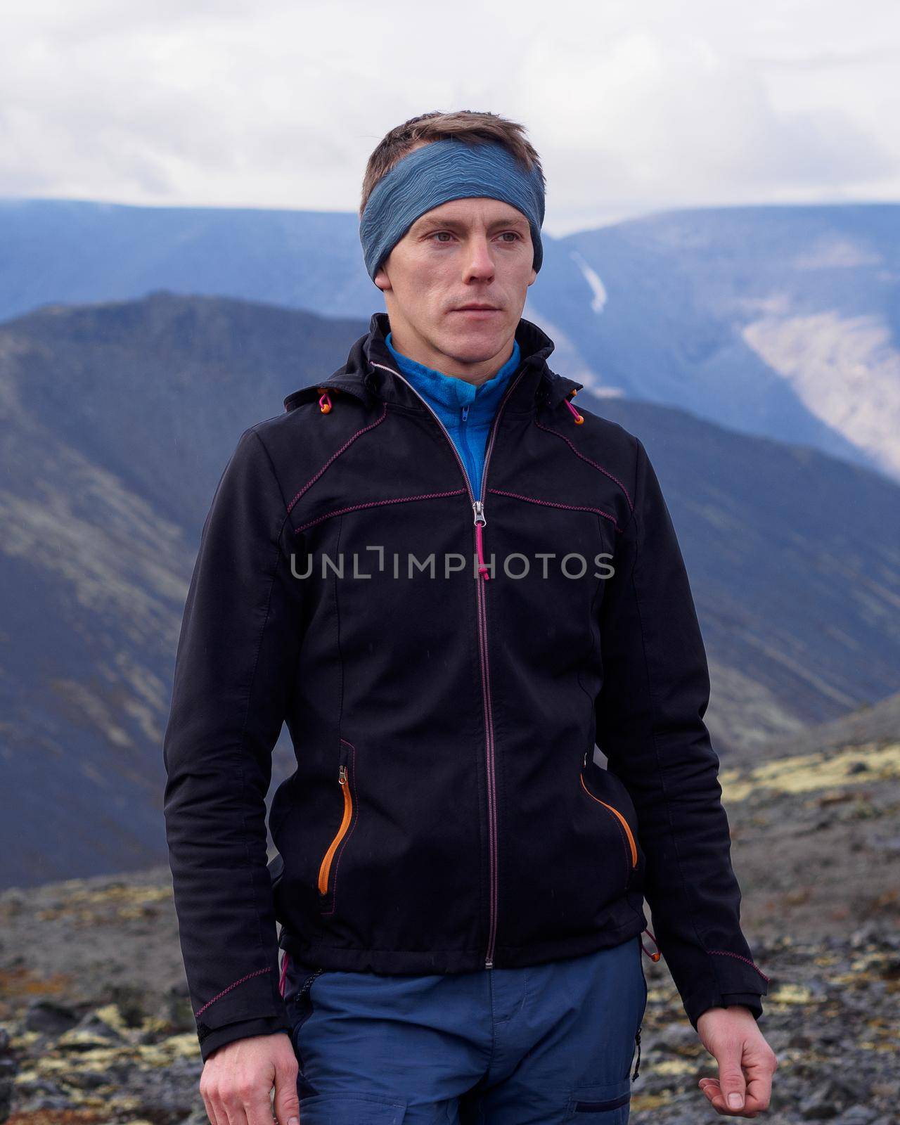 a young man with trekking poles in a bandana stands against the backdrop of mountains. photo