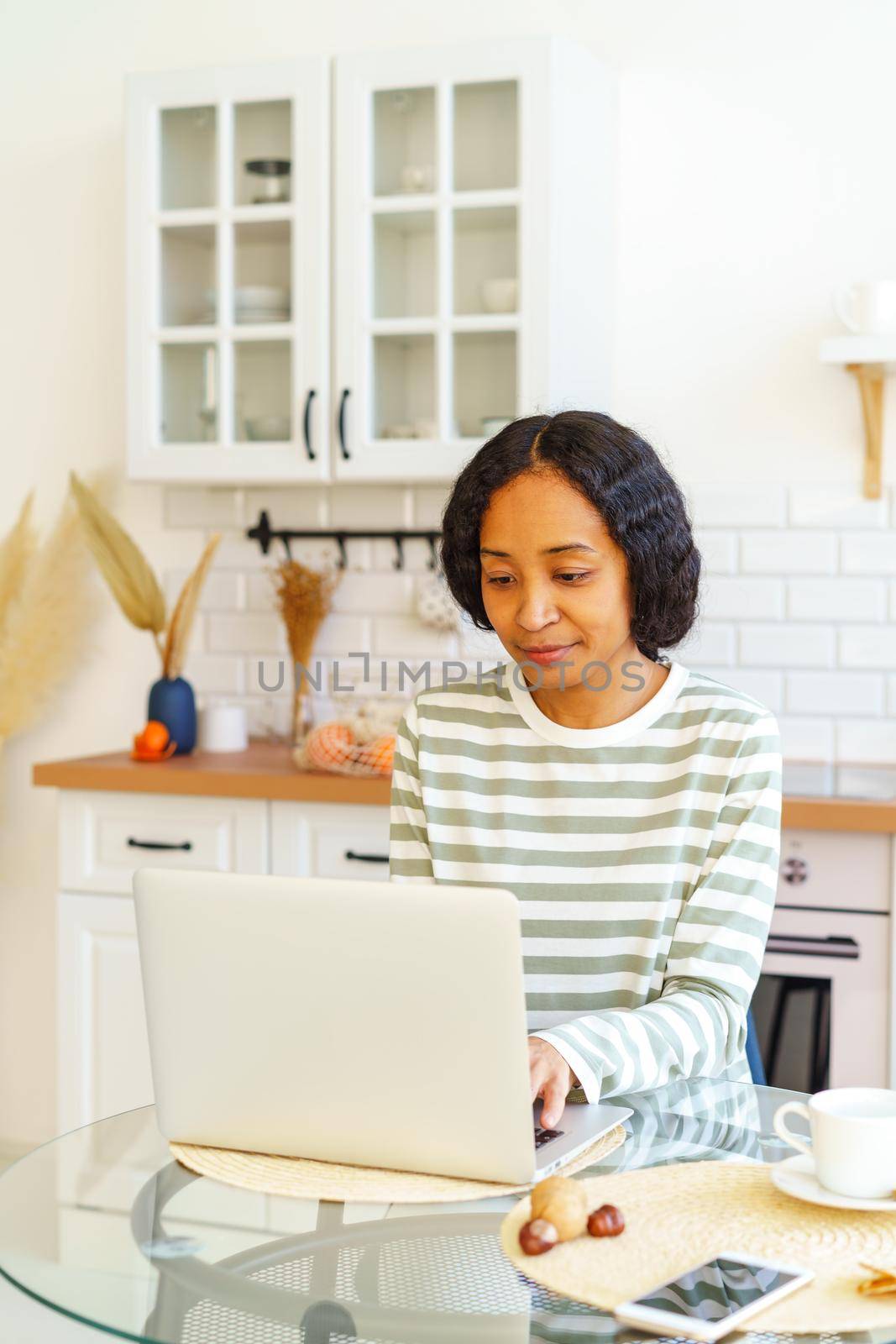 African-American woman working on laptop while sitting in dining room. Concentrated on remote work from home. Concept of telecommuting and teleworking in kitchen