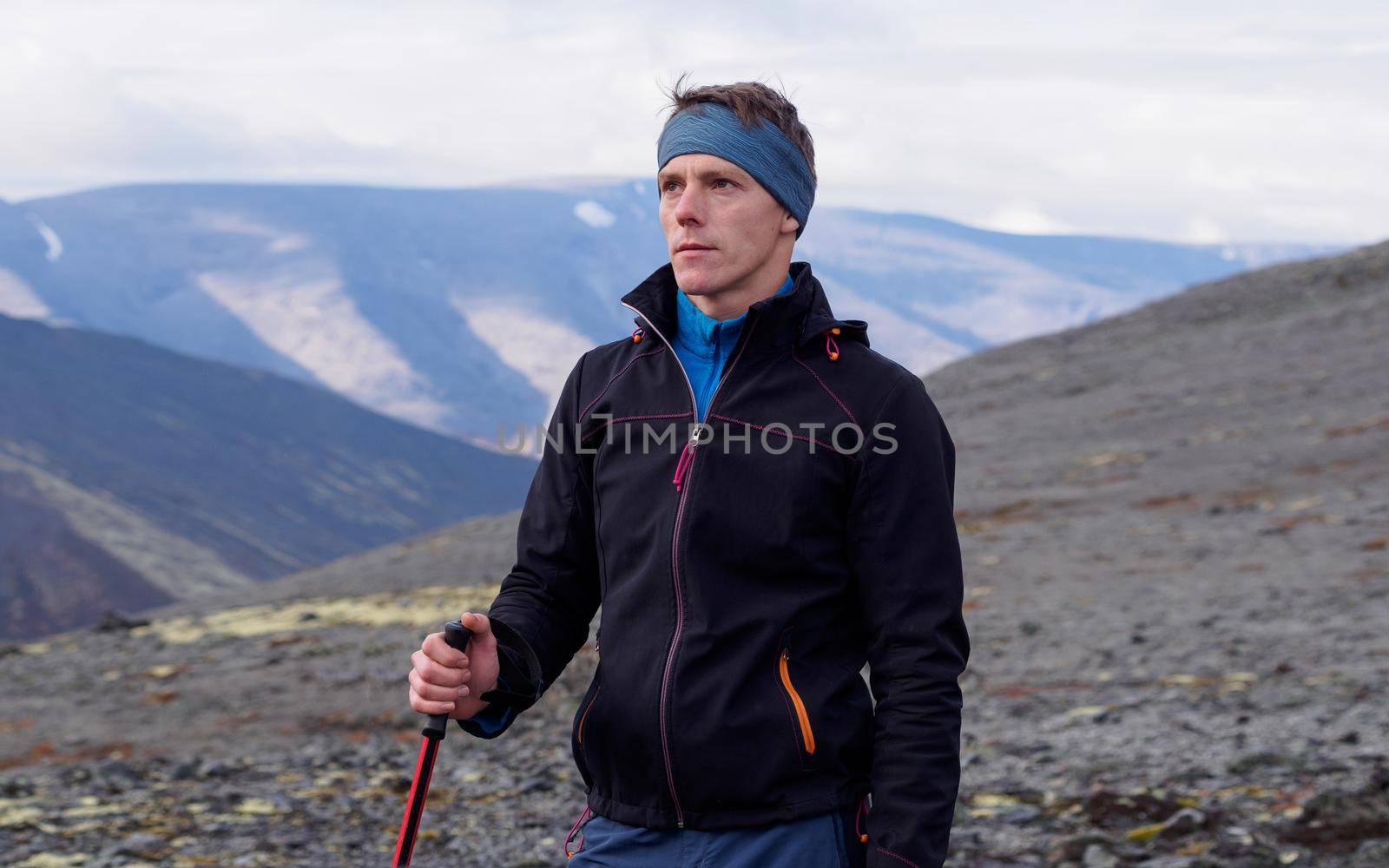 a young man with trekking poles in a bandana stands against the backdrop of mountains. photo