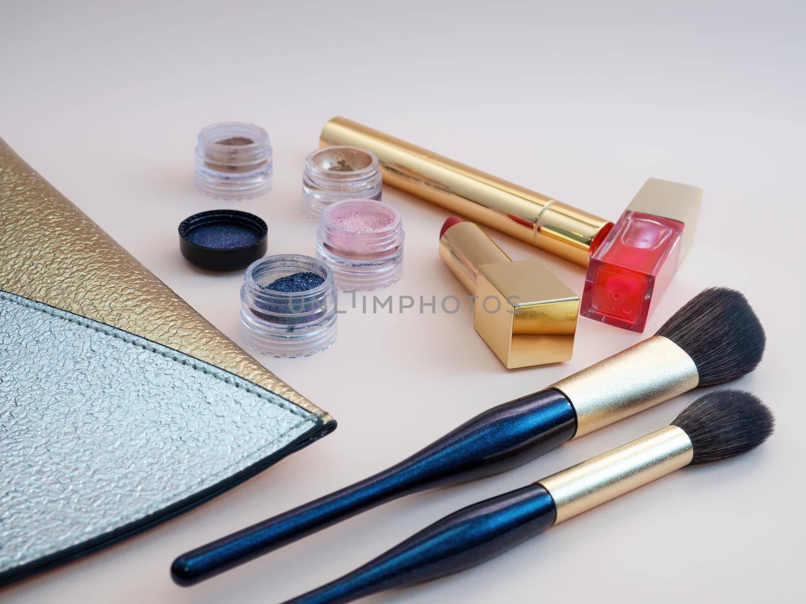 Top view of cosmetics standing out from golden makeup bag on pink background by Andre1ns
